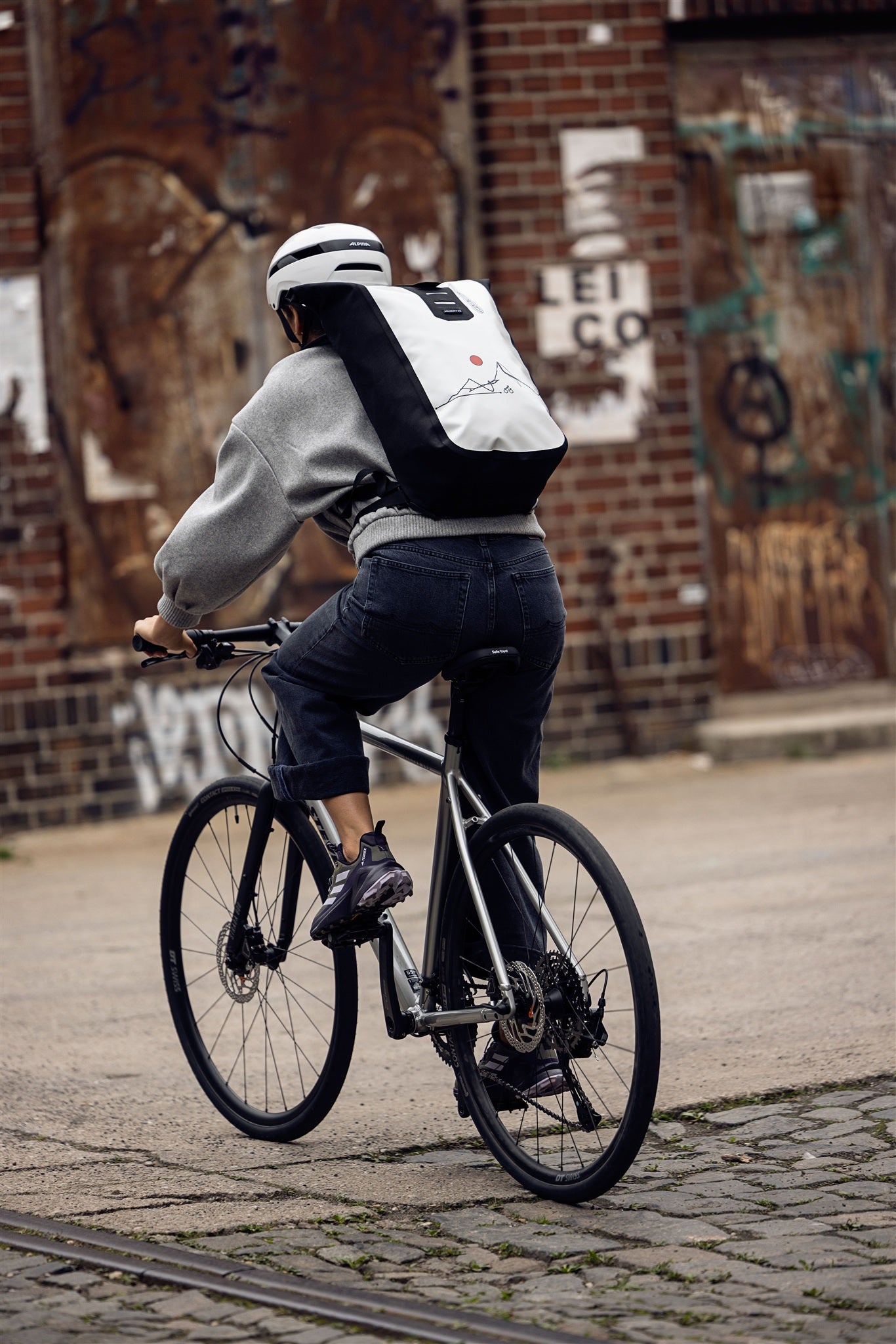 Femme assise sur escalier métallique avec sac à dos ORTLIEB Velocity Design blanc et noir avec soleil rouge