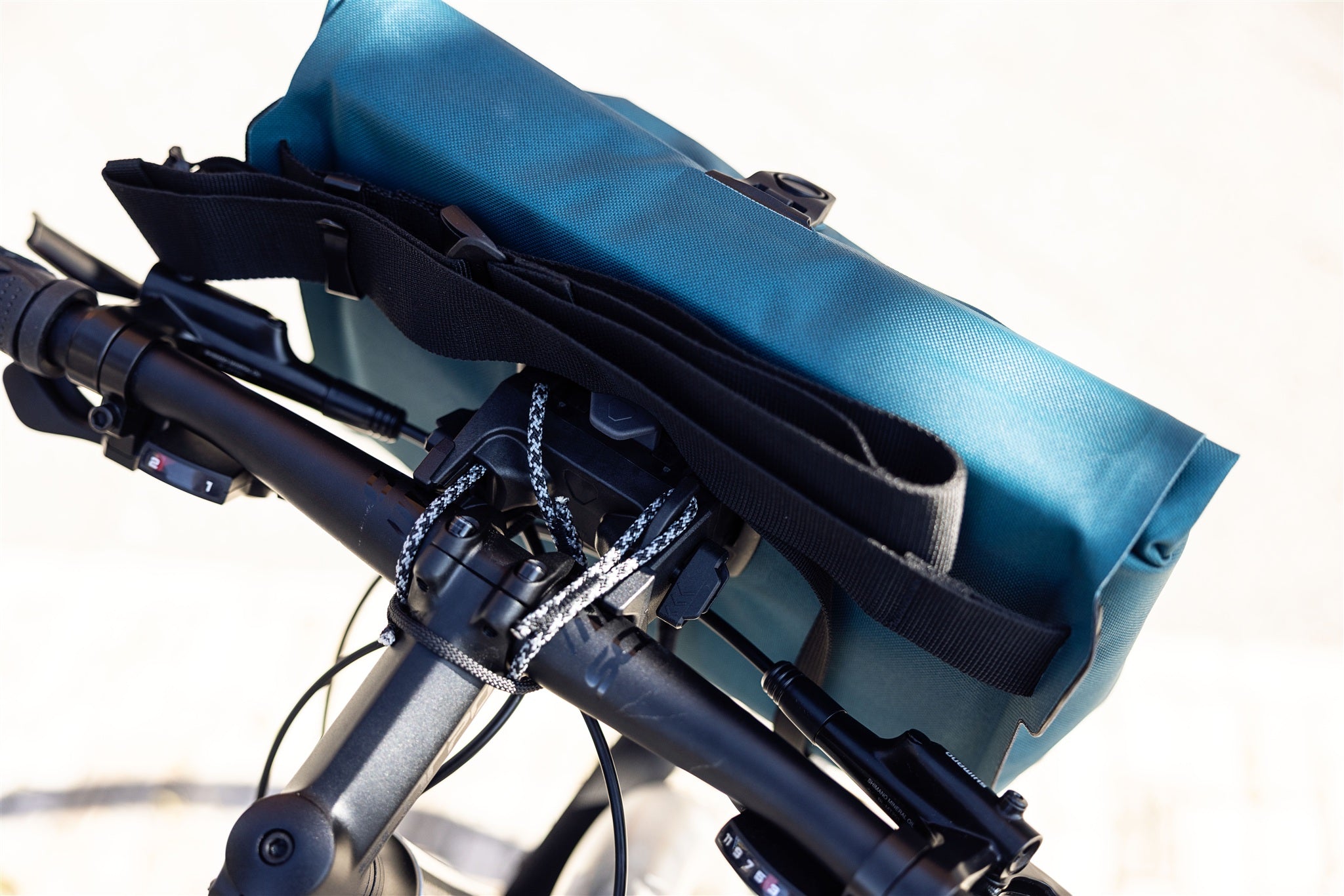 Vue détaillée du sac de guidon ORTLIEB Velo-Sling Flex couleur pétrole avec fixation Bar-Lock en tissu imperméable sur le vélo.