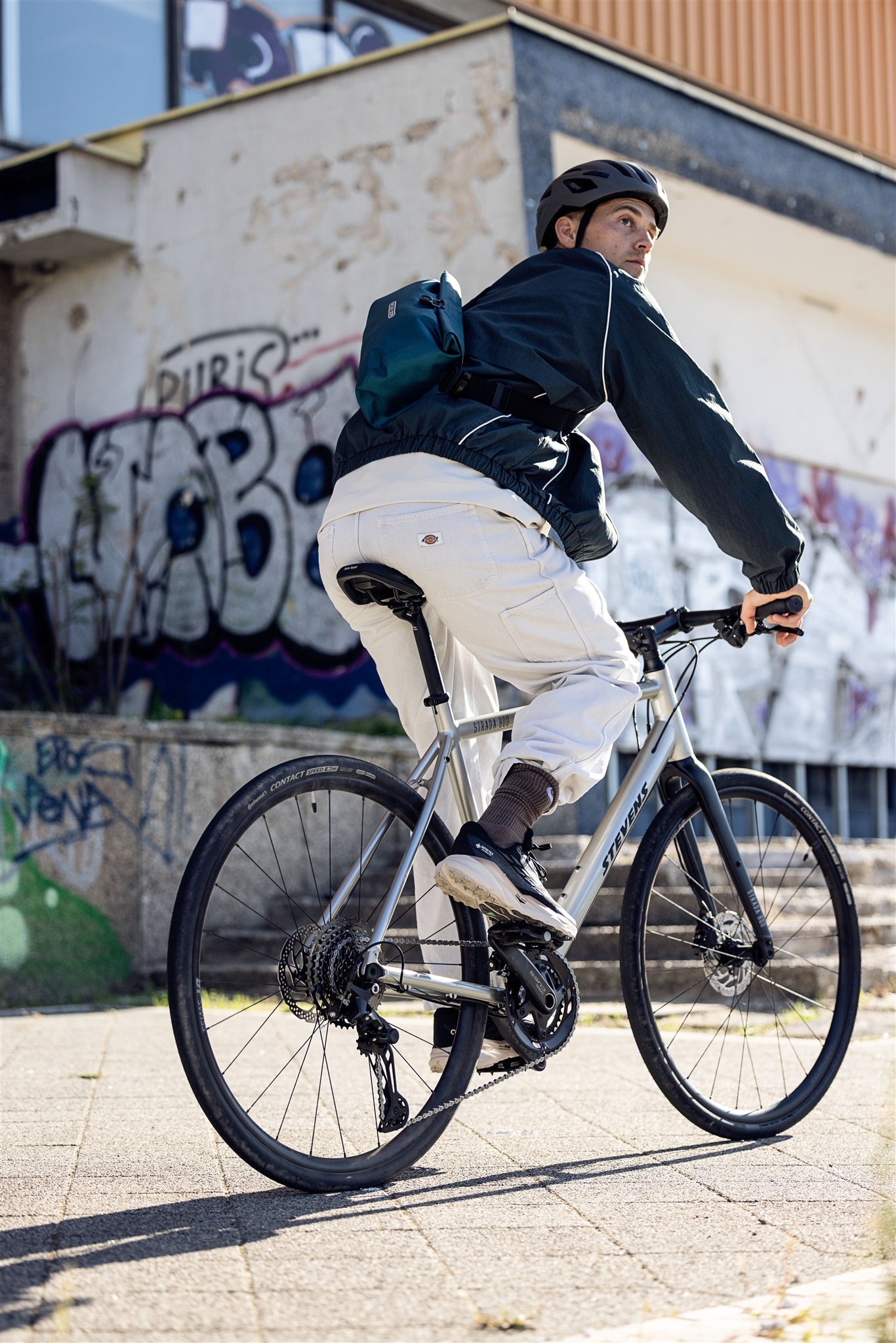 Cycliste portant la sacoche de taille ORTLIEB Velo-Sling Flex couleur pétrole dans un décor urbain graffité.